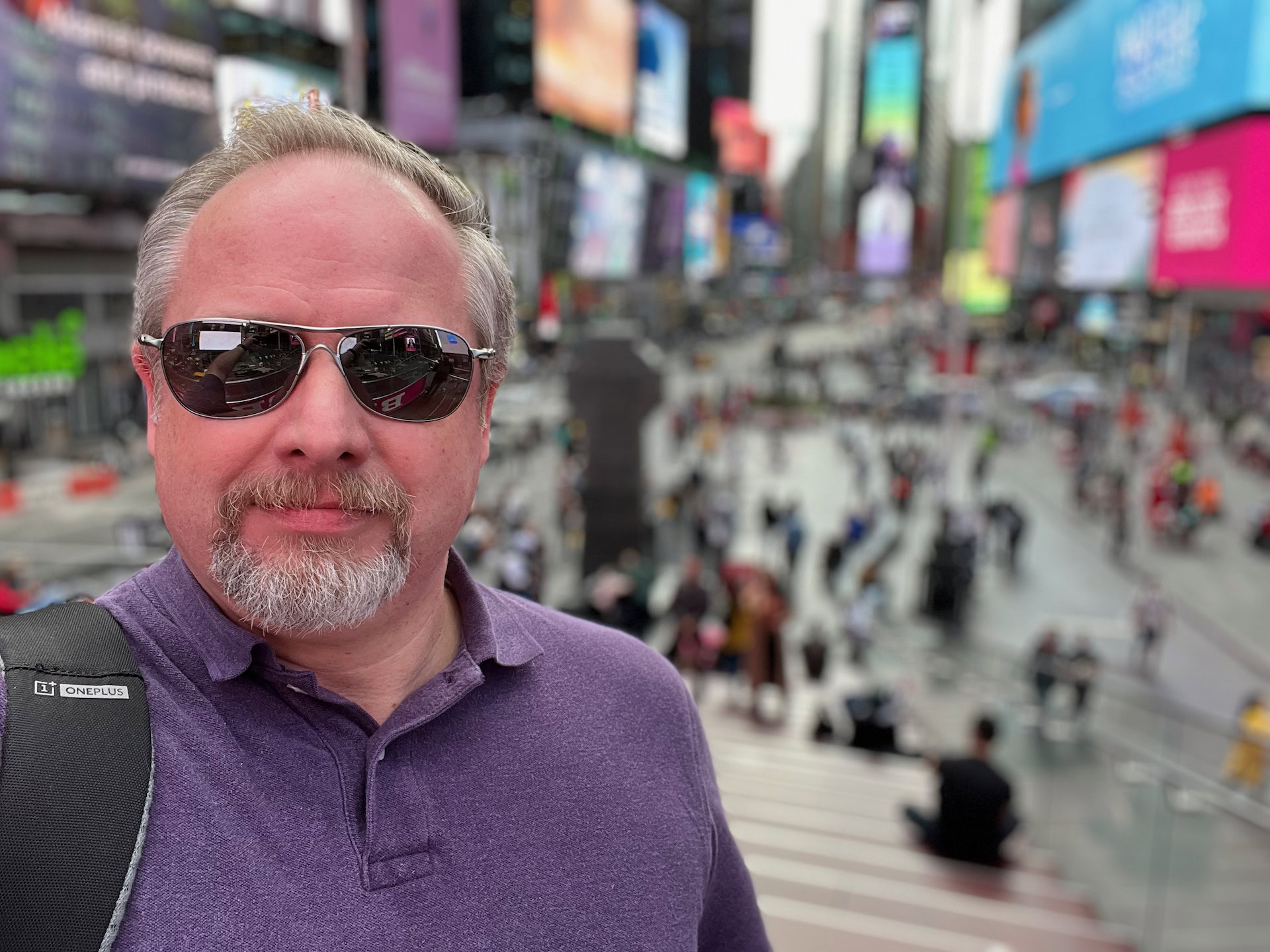 Apple iPhone 13 photo sample Times Square portrait of a man with light colored hair and beard wearing a purple top and black shades