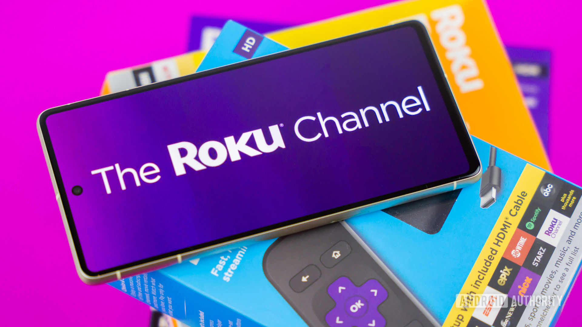 Stock photo of The Roku Channel logo on phone next to Roku boxes 7 Stock photo of The Roku Channel logo on phone next to Roku boxes 7