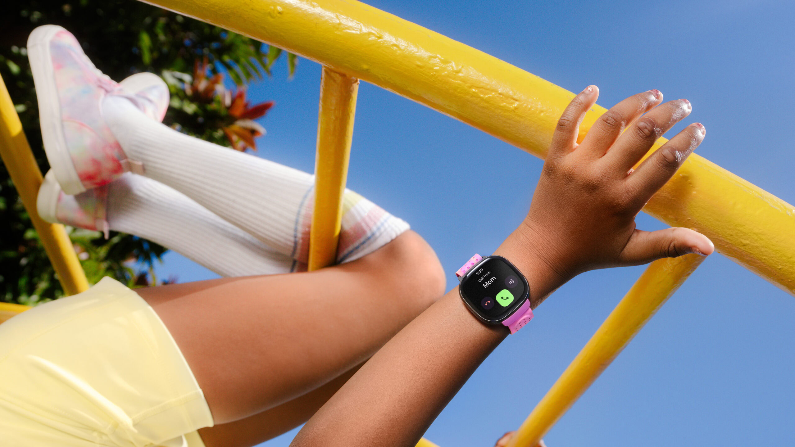 Fitbit Ace LTE playground A child wearing a Fitbit Ace LTE hangs from a piece of playground equipment.